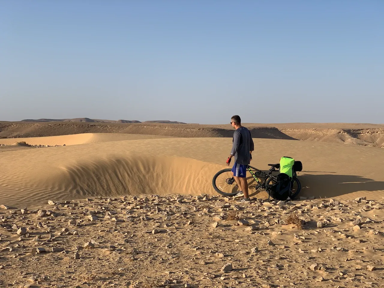 Dmytro standing next to a loaded touring bike on a sand dune in the Negev desert.