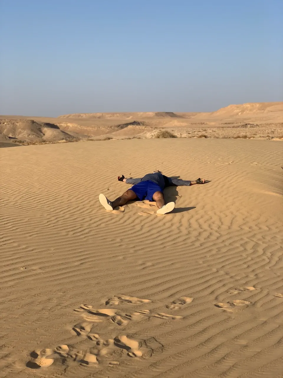 Dmytro lying spread-eagle on a rippled sand dune, exhausted.